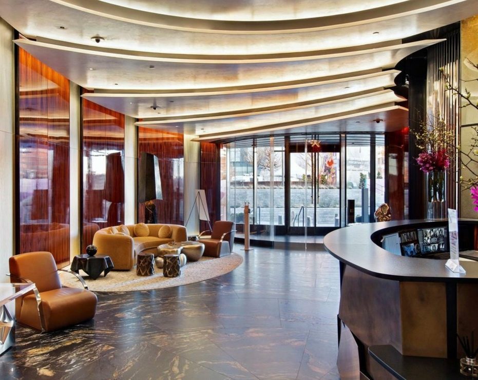 Le lobby de l'hôtel du 35 Hudson Yards : parois de bois à haut lustre, plafond en lames courbes, fauteuils de cuir