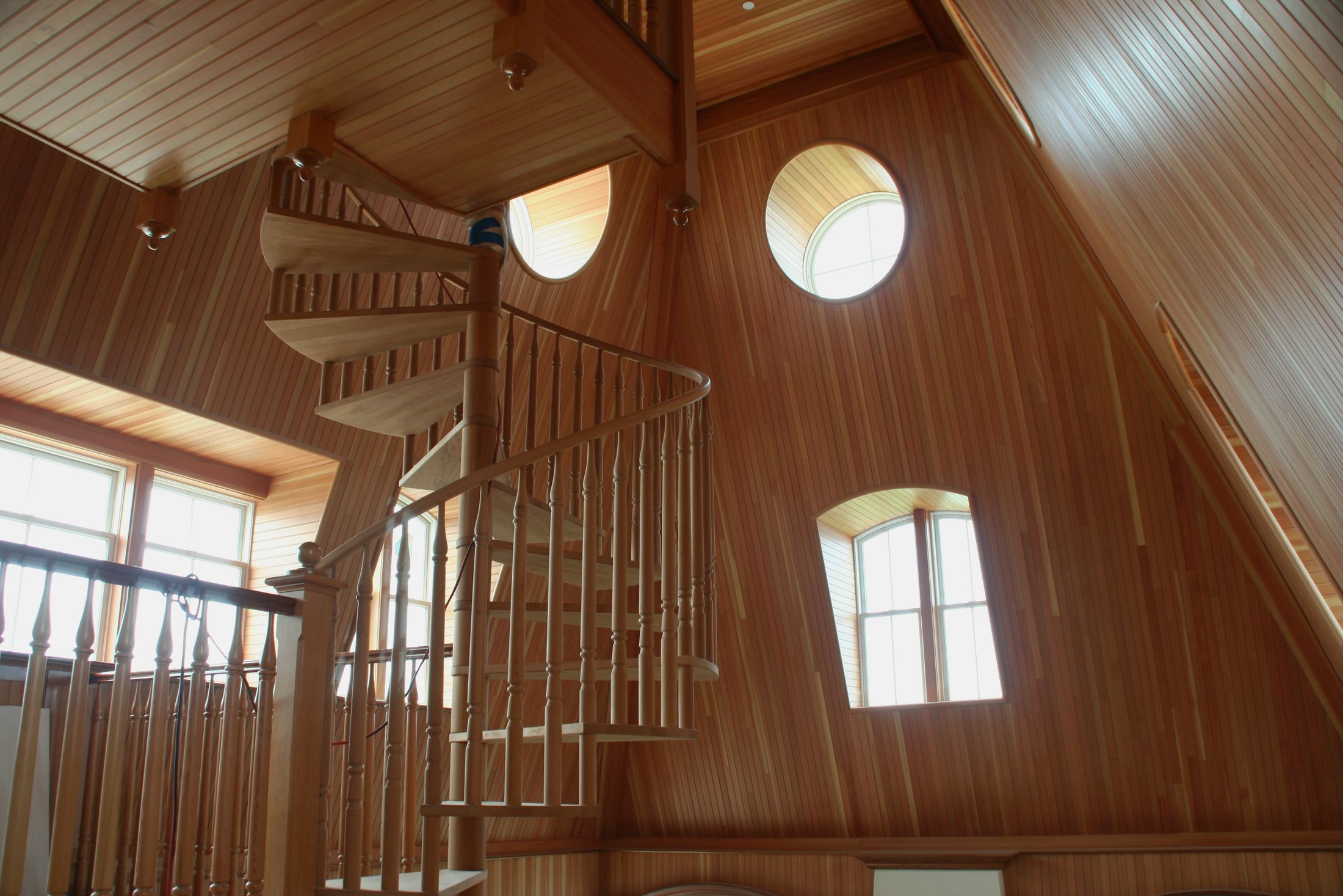 Un escalier en colimaçon dans une pièce toute lambrissée de bois clair, avec des fenêtres rondes, à l'Ocean House