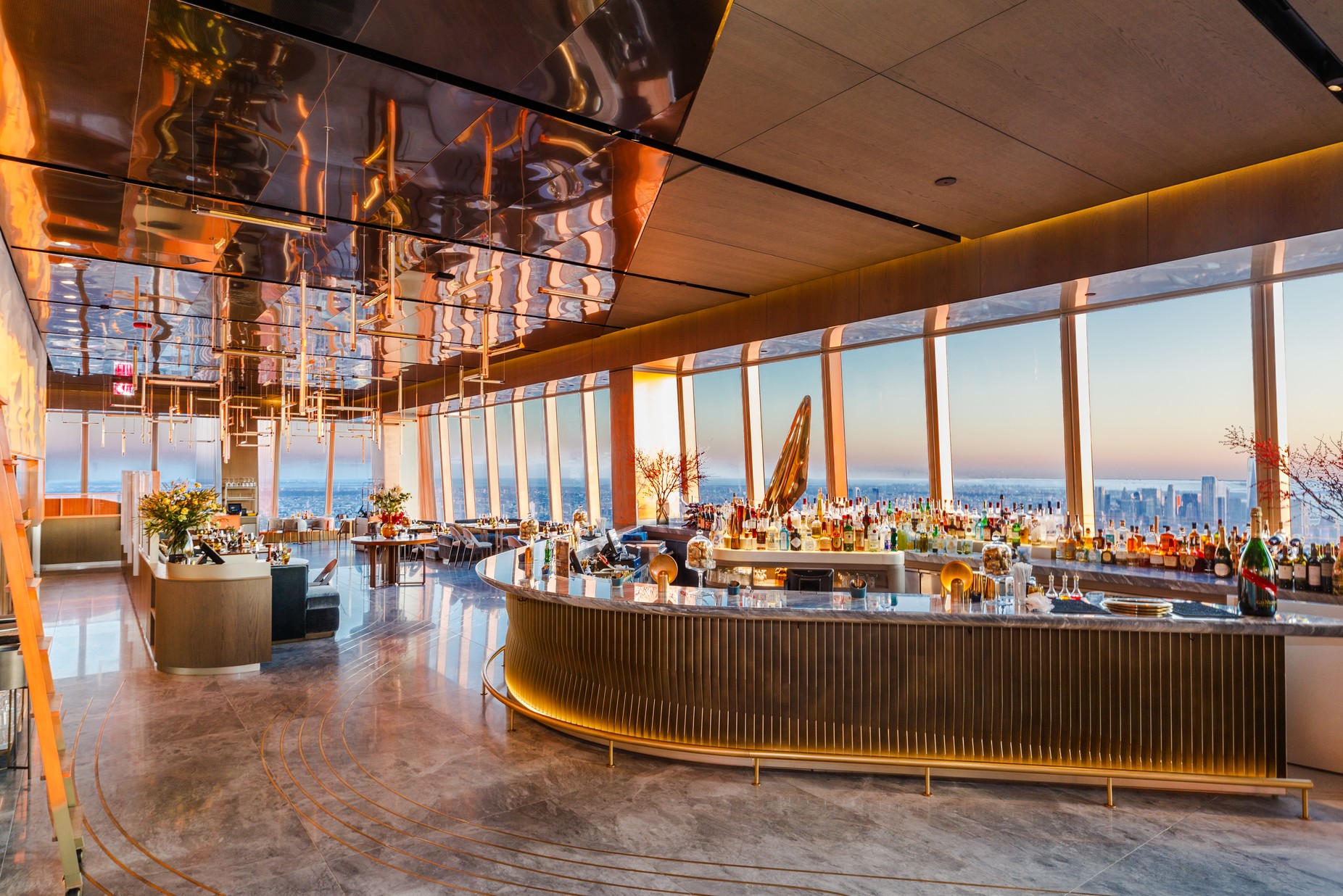Le bar du restaurant Peak, au 30 Hudson Yards à New York : le comptoir courbe, le plafond, la baie vitrée sur Manhattan au coucher du soleil